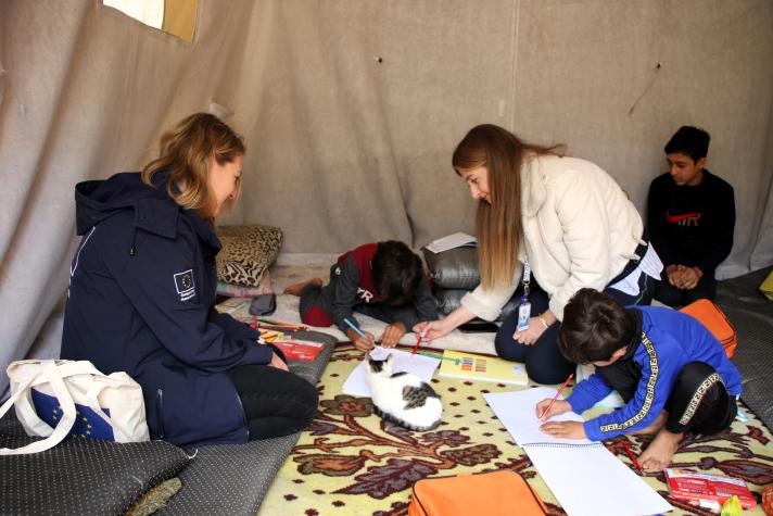 Some aid workers sitting in the tent together with some children while looking at drawings and school work.