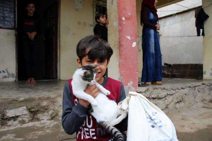 A boy holding a cat in his arms while standing in front of the house.
