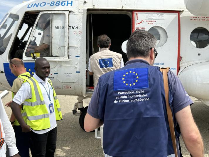 People stepping into a helicopter, the last one wearing a vest with the European flag and the text European Humanitarian Aid.