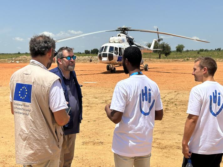 4 aid workers talking, a helicopter in the background.