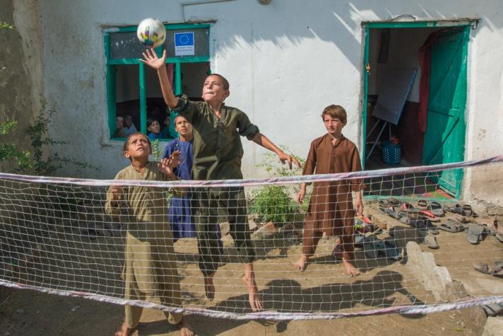 A group of children playing with a ball, in front there is a tennis net.