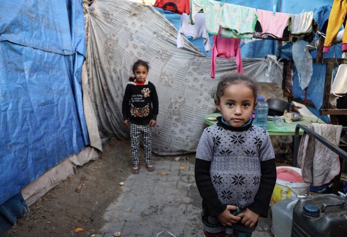 2 children standing inbetween makeshift tents. A washing line with clothes in the background.