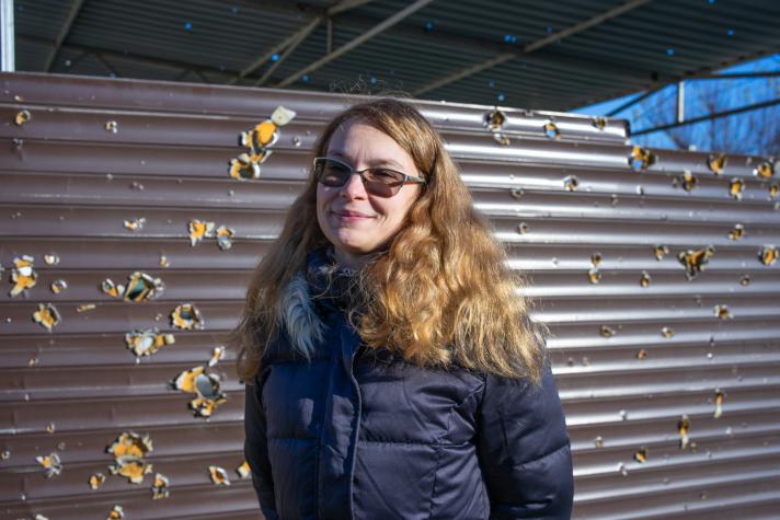 Nataliia, wearing sun glasses, standing outside in front of a garden fence.