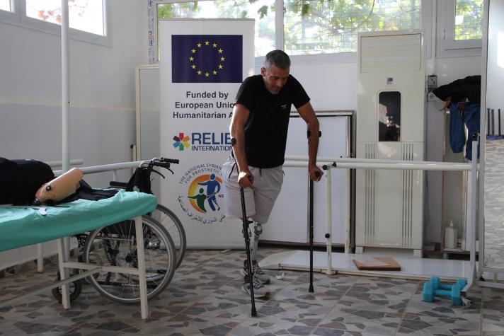 Mustafa learning to walk with protheses. A bench and other equipment shown in the room.