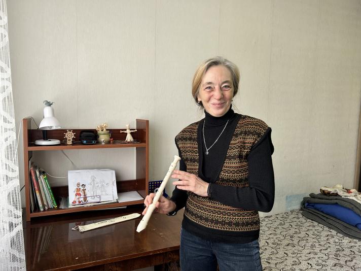 Yuliia, in her daughter´s room, holding a  blockflute. In the background a bed and a desk.