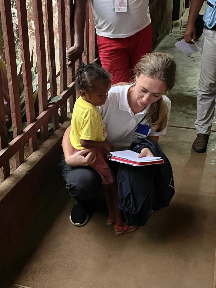 An aid worker holding a child on her lap while reading a book.