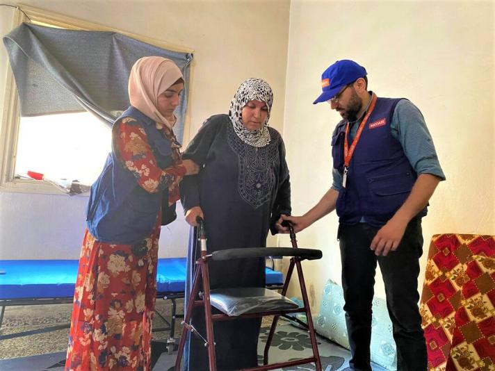 Health workers next to Rabiea holding on to her rollator.