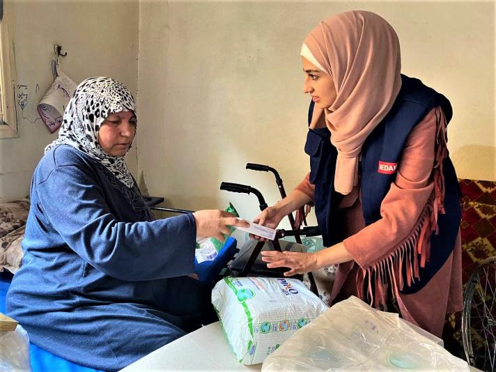 Rabiea sitting on a chair while a health worker hands her a hygiene pack.