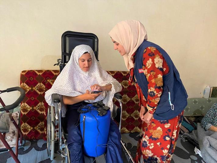 Momena seated in her wheelchair talking to a health worker.