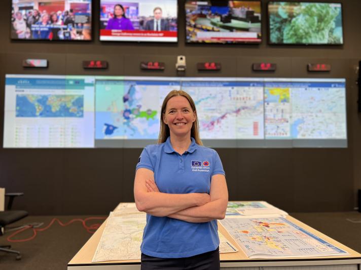 Claire in the EU’s Emergency Response Coordination Centre in Brussels, large screens displaying maps and news channels in the background.