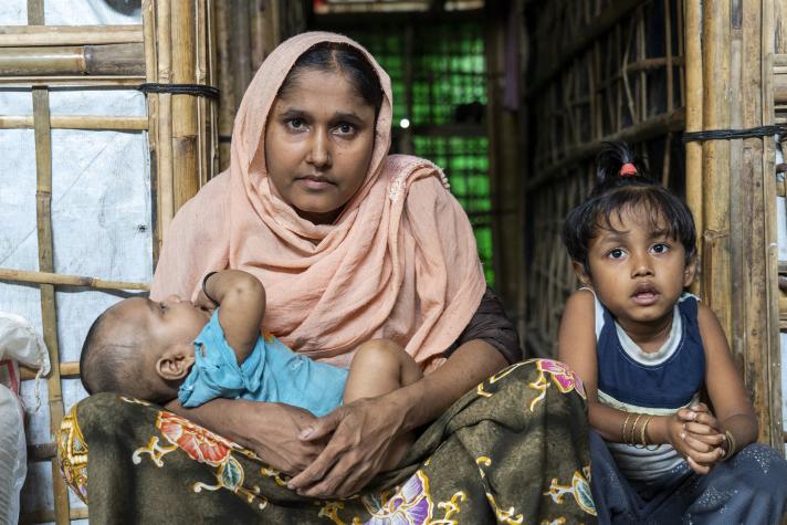 Rokeya holding a baby in her arms, next to her sits her other daughter.