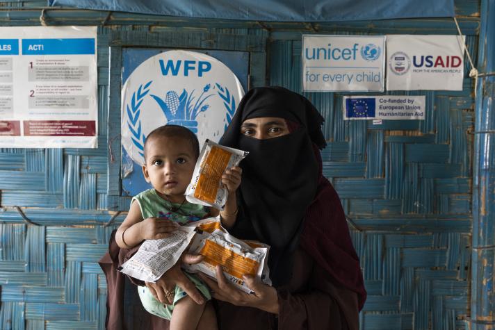 A woman holding a young child in her arms together with specialised nutritious food packs.