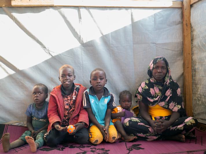 Noura and her family sitting inside the emergency shelter. A white canvas/wall in the back.