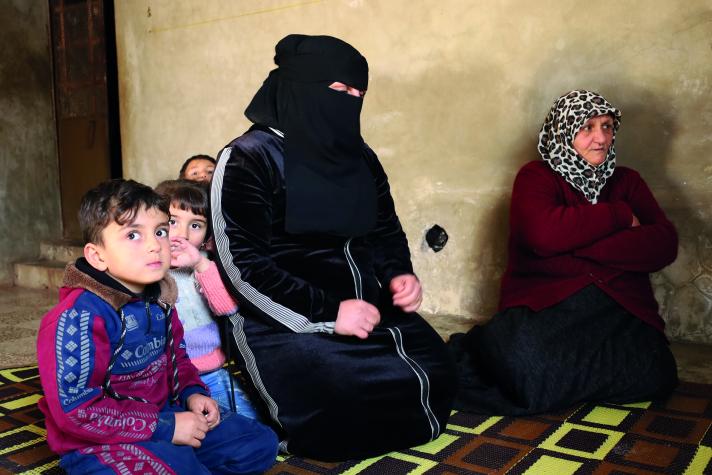 Muna sitting in her house with on the right her mother and on the left her 2 children.