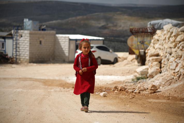 A child wearing a red dress walking in a street.
