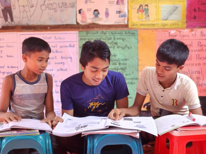 Robi sitting together with Kamal and Jahidur in the class room, looking and writing in a workbook.