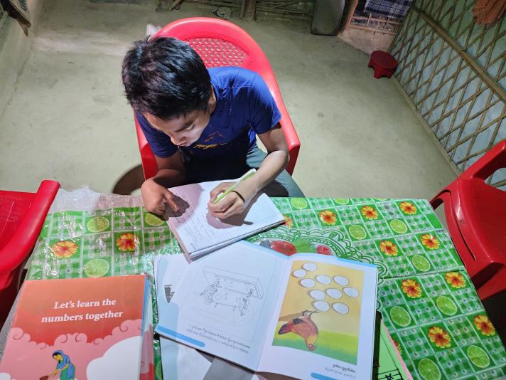 Robi seated at a table with books from school all over the table top.