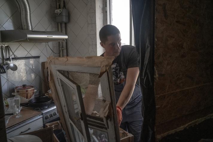 A builder working in a kitchen, holding a broken window to be replaced.