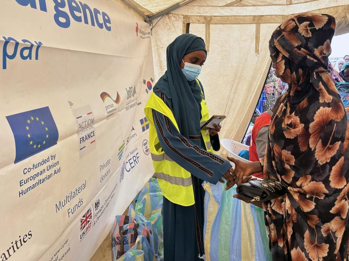 A woman, standing in a tent, receiving an emergency food ration from an aid worker.