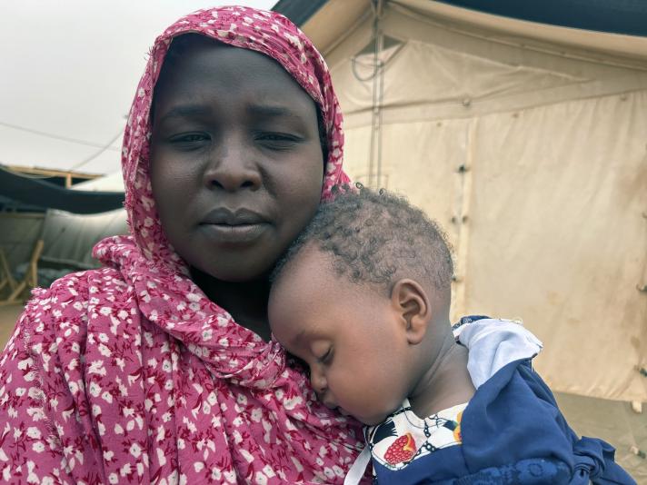 Saad holding her 9-month-old daughter in her arms, standing in front of a tent.