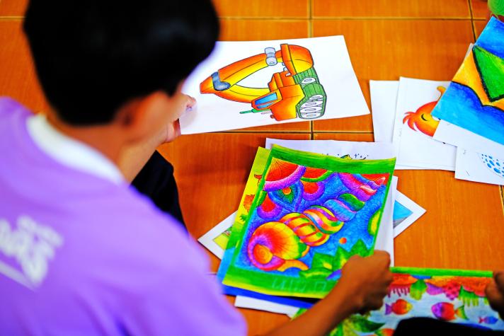 A table full with colourful drawings some being held by a young person.