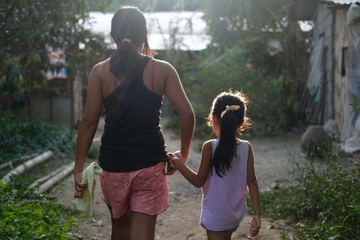 Miriam and her daughter walking hand in hand, seen from the back.