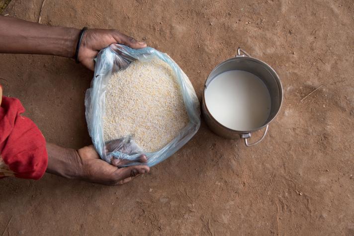 Hands holding a bag of maize powder next to it a pan with milk, seen from above.