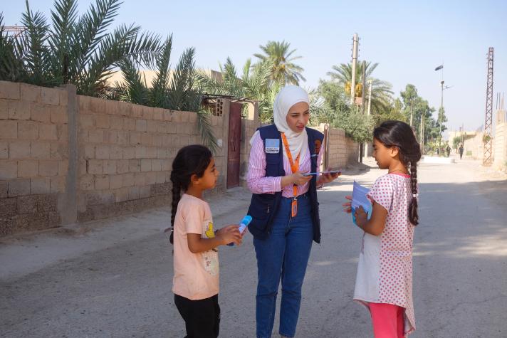 2 children talking with an aid worker on a street.