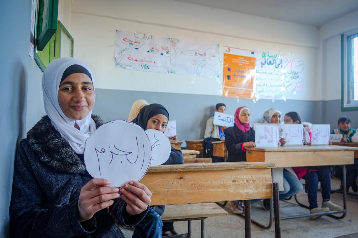 A groupd of children in a classroom holding up signs.