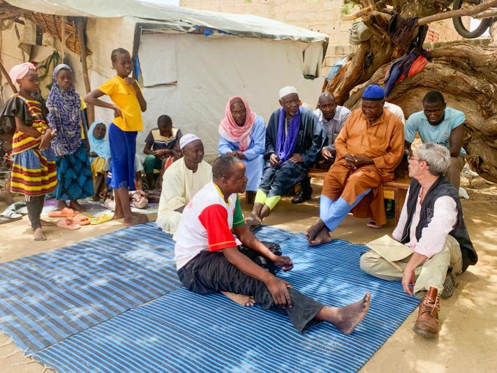 An aid worker sitting with locals outside under a tree.