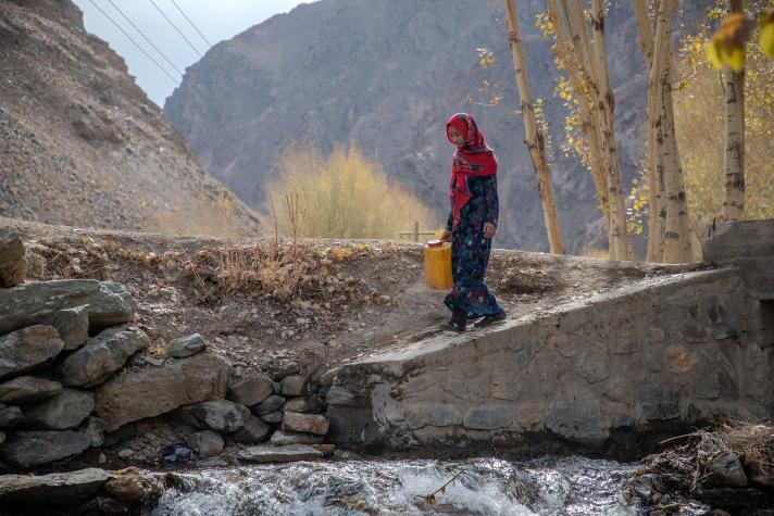 Rozama walking towards a river with a gallon to collect water.