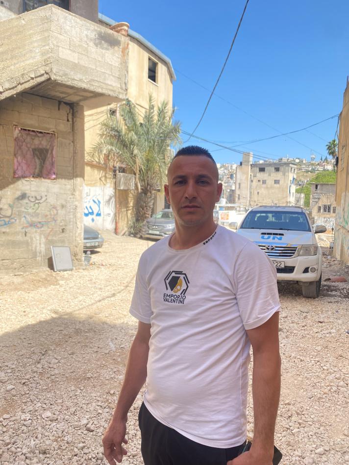 Eyad standing in a street, in the back a car and building.