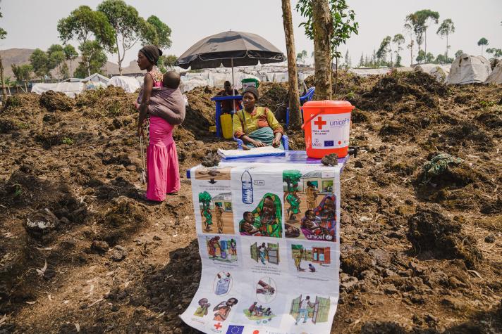 People sitting outside, in front a poster explaining hygiene practices.