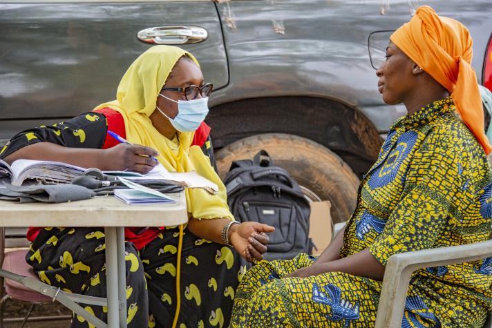 A midwife speaking to a pregnant women while seated at a table outside. 