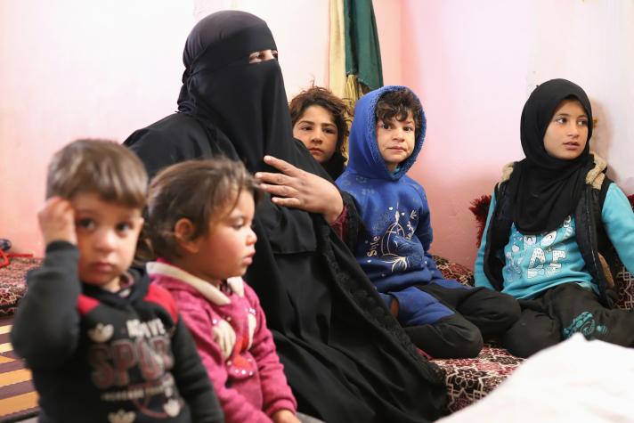 A mother with 5 children around her sitting in a tent.