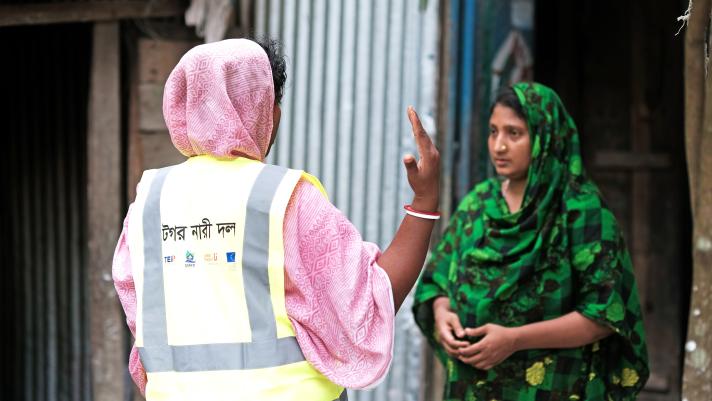 Sajia Akhter standing in her doorway, an aid worker is talking with her.