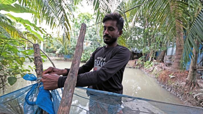 Billal uses mesh to cover his fishpond, in the back a row of trees.