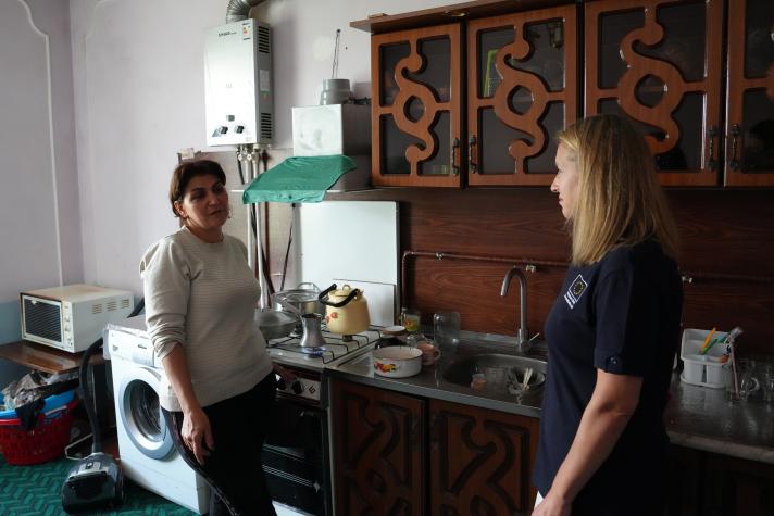 Evelina talking to an aid worker, standing in her kitchen.