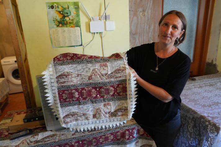 Alvard holding up an embroidery while seated in her living room.