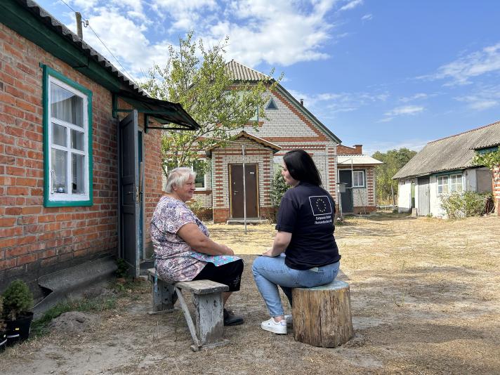 Paraskoviia and Ivanna sitting outside the house on wood blocks.