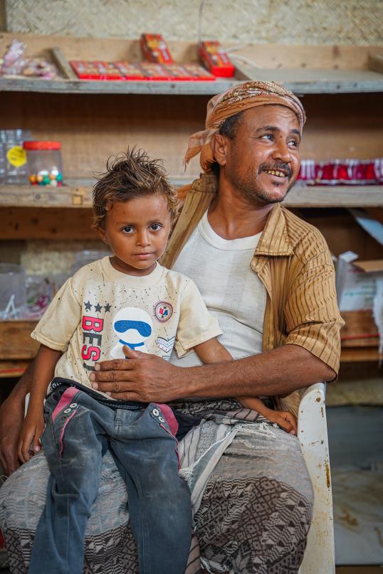Hasan sitting in his shop with a boy on his knee