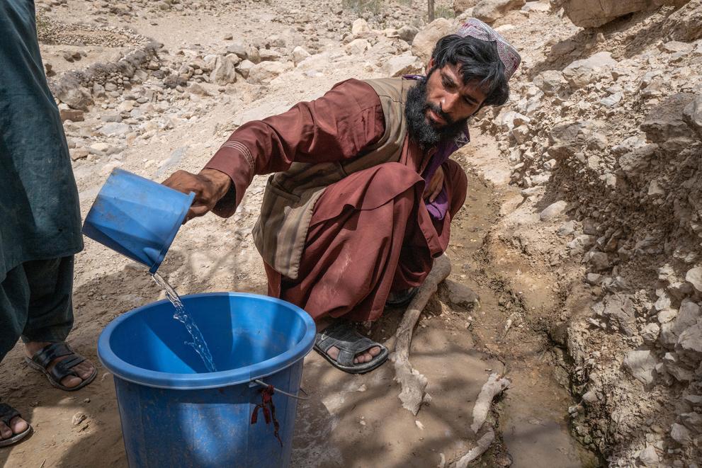 Muhammad scoops water into a bucket with a small plastic cup