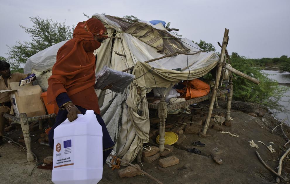 Woman carrying a water tank walking in front of her makeshift shelter