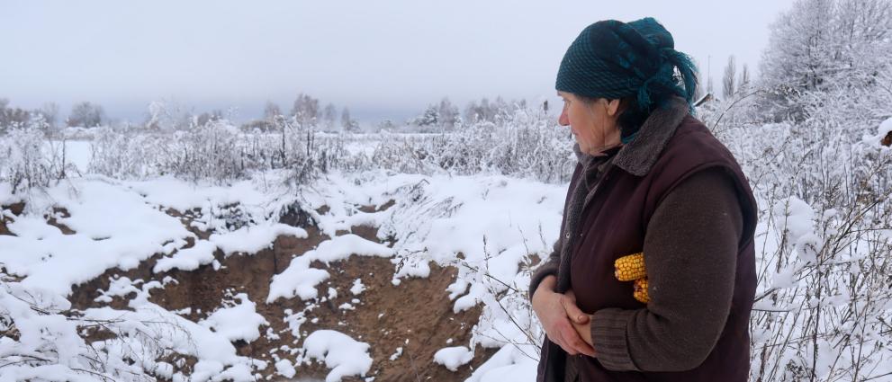 A woman standing in a snowy landscape holding corn under her arm.