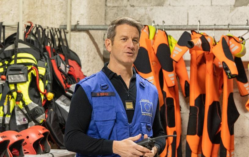 Alain Biasci holding a walkie talkie and standing in front of safety gear