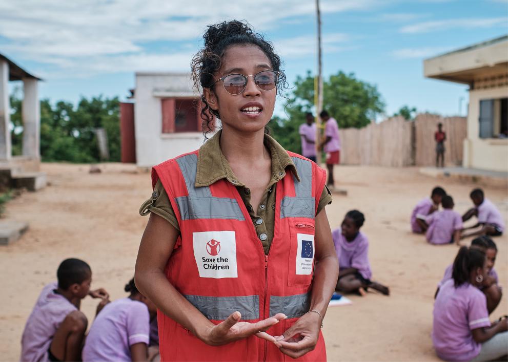 Mirana R’Abel in a Save the Children vest with children in a school yard