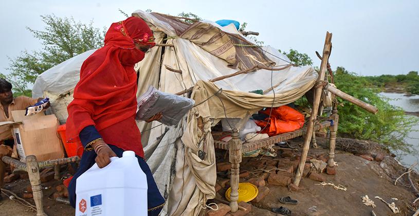 A woman carrying a water container walking in front of a temporary shelter