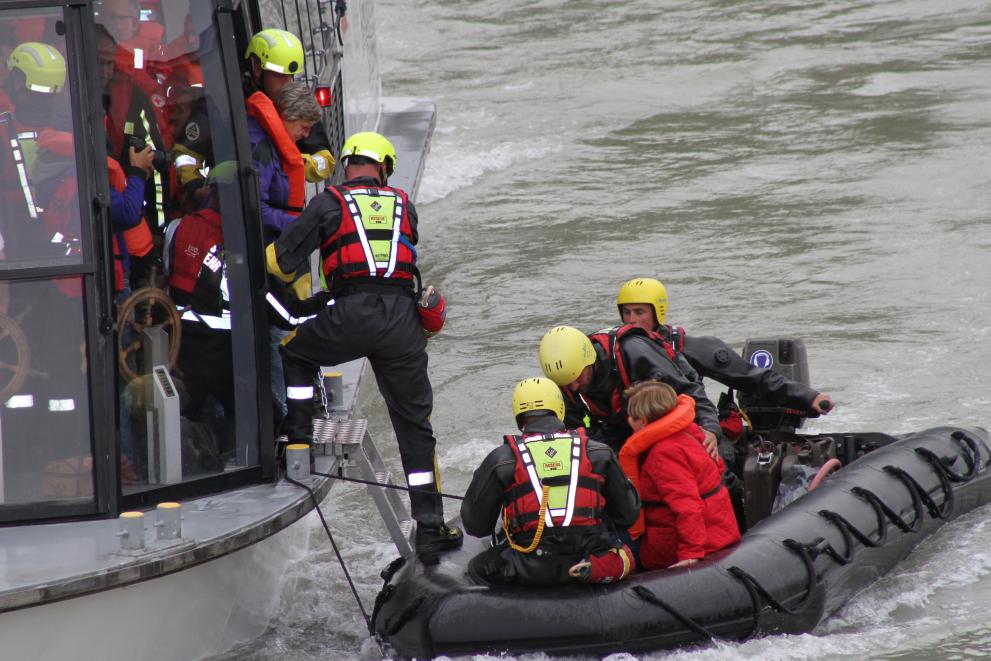 People wearing safety gear stepping from a boat into a smaller rubber dinghy