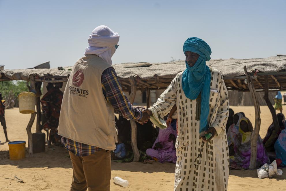 Aid worker shaking hands with a man, in the background a sheltered space in the desert.