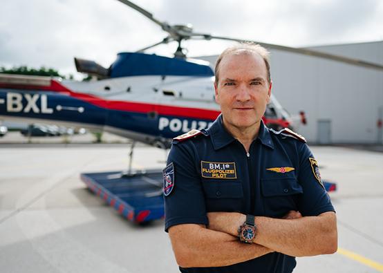 man in pilot's uniform standing in front of a police helicopter